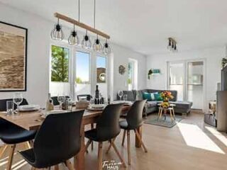 A modern dining and living area with a large dining table, stylish black chairs, and chic pendant lights, leading to a lounge area with a comfortable sofa.