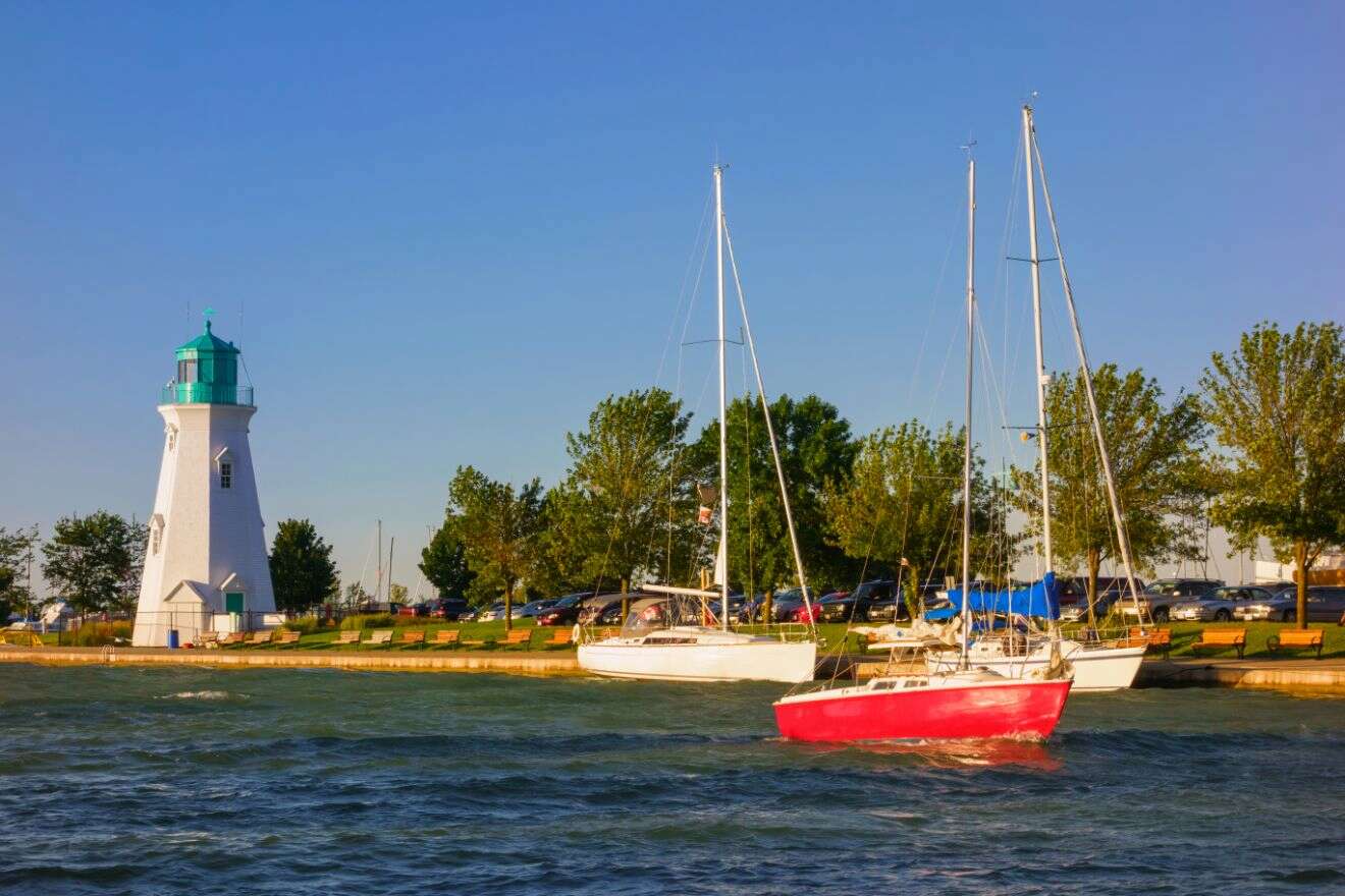 Sailboats moored near a white lighthouse at a marina in St. Catharines, with a calm blue waterfront and clear skies