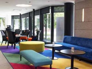 Hotel lobby with colorful modern furniture on a multicolored rug and large windows offering natural light.