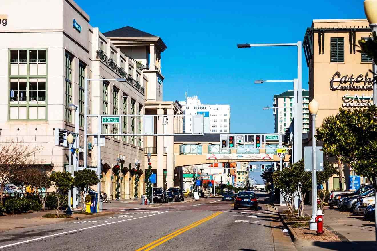 A street-level view of a busy Virginia Beach street lined with hotels and restaurants, under a clear blue sky