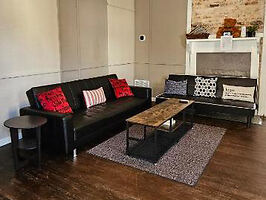 Urban living space with two black sofas with red and black patterned pillows, a rustic coffee table, and a vintage fireplace mantle