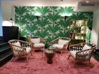 Lush lounge area with rattan chairs, striking green leaf-patterned wallpaper, and a plush red carpet