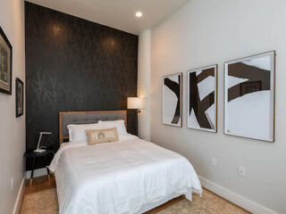 Minimalist bedroom design featuring a single bed with 'Home' pillow, abstract wall art, and a black feature wall