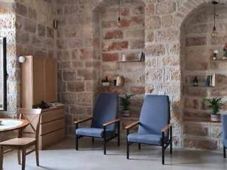 Stylish rustic interior with exposed brick walls, two navy blue upholstered chairs, and a wooden cabinet with books and decorative items.