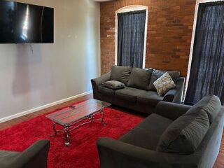 A modern living room featuring a large grey sofa, a glass coffee table on a vibrant red rug, and a brick accent wall