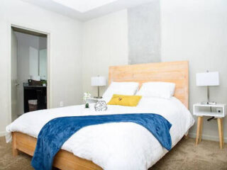 Bedroom with a simple aesthetic featuring a wooden headboard, white and blue bedding, and a small bedside table