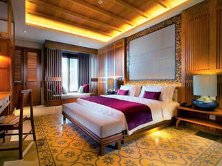 Elegant hotel room with a traditional touch, featuring a carved wooden headboard, rich purple bedding, and patterned floor tiles, blending luxury with local design elements