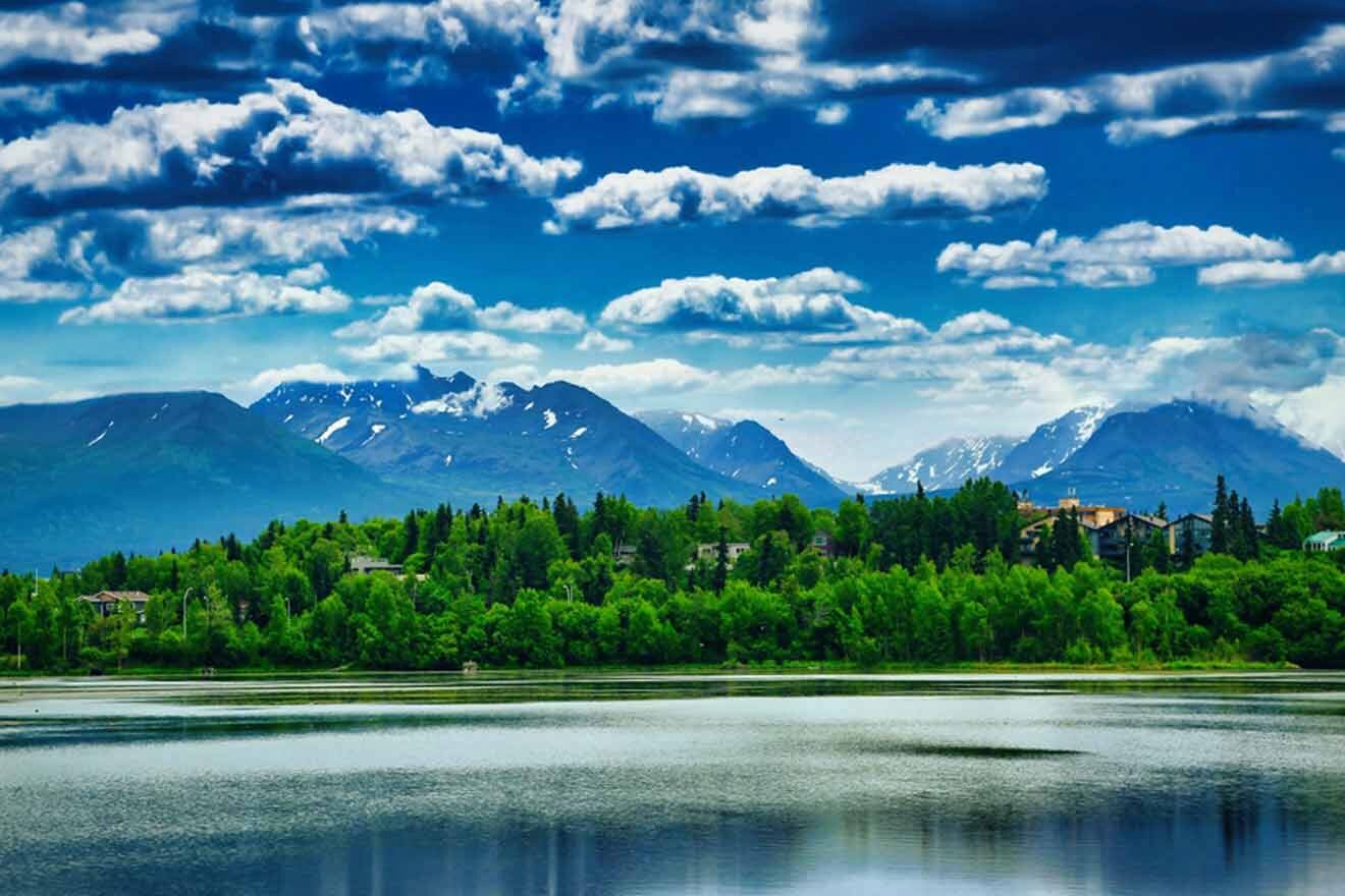 A vibrant landscape of a lake with calm waters, lush greenery, and the Alaskan mountain range under a dynamic cloud-filled sky.