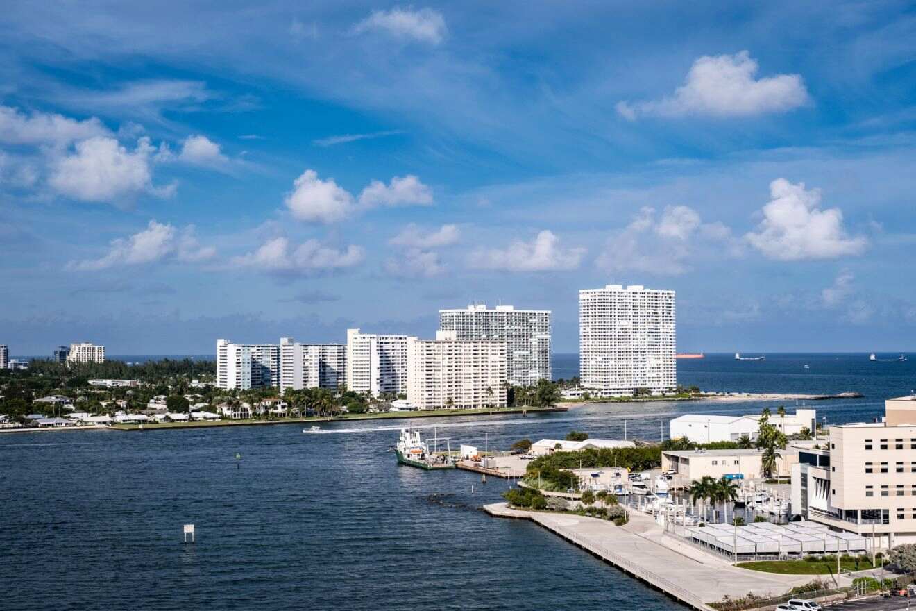 Coastal city view from a harbor, featuring white high-rise buildings against a backdrop of blue sky and sea