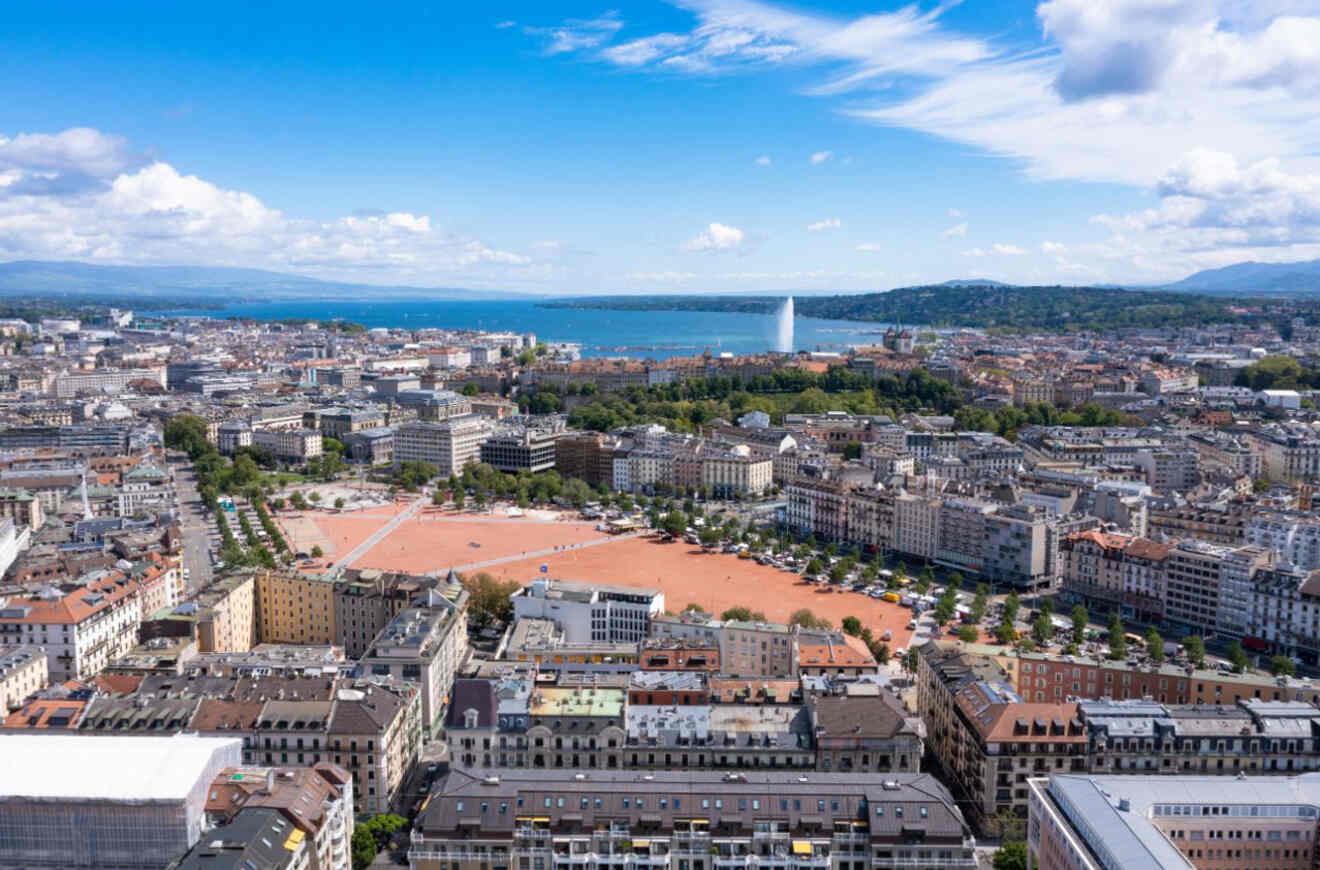 Aerial view of Geneva cityscape, highlighting the red rooftops, open squares, and the Jet d'Eau fountain with Lake Geneva in the background