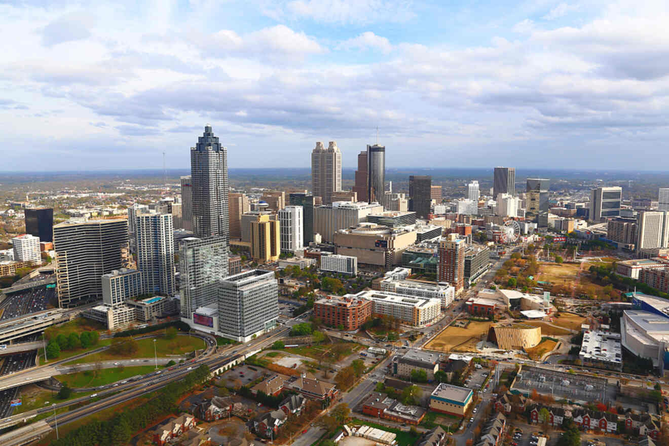 Aerial view of downtown Atlanta, showcasing skyscrapers, city streets, and scattered green spaces under a cloudy sky