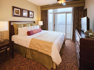 Elegant hotel bedroom with a king-sized bed, decorative pillows, a ceiling fan, and balcony access with ocean views