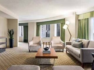 A spacious hotel suite living area with plush seating, modern decor, and floor-to-ceiling windows providing ample natural light.
