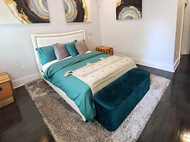 Sophisticated bedroom with a teal and white color scheme, featuring an elegant bed, plush teal bench, and abstract wall art