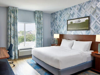 Hotel bedroom with a king-size bed, patterned wallpaper, and a framed picture above the headboard