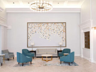 Elegant hotel lobby with a large artistic wall decoration, comfortable teal armchairs, a cream sofa, and a luxurious chandelier