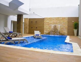 Indoor hotel pool with a cascading water feature, surrounded by lounge chairs