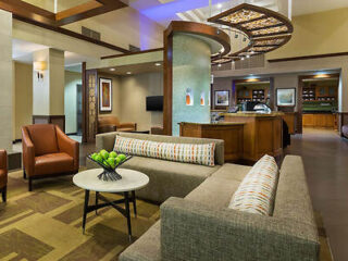 Warm and welcoming hotel lobby of Hyatt Place featuring earth-toned furnishings, a statement ceiling light, and a hospitality desk