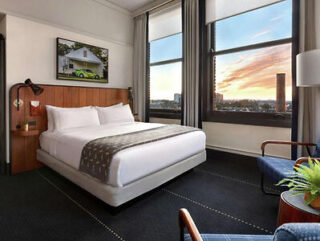 A contemporary hotel room with a sleek design, featuring a comfortable bed, modern furniture, and a stunning view of the cityscape at dusk