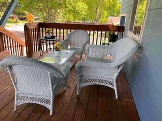 A homey porch with white wicker furniture and a glass top table, set for a relaxing outdoor experience.