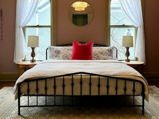 Chic bedroom with elegant light fixtures, white drapes, a patterned rug, and a red accent pillow on the bed