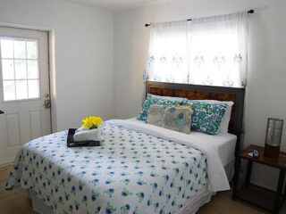 Cozy bedroom with a floral patterned blue bedspread, wooden headboard, and matching white curtains and bedside table