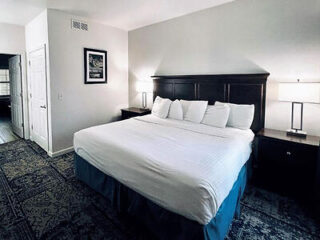 A spacious and well-lit hotel bedroom with a large king-size bed, crisp white linens, and dark wood nightstands
