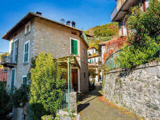 Charming stone house with green shutters, nestled in a picturesque alley with lush greenery in a traditional Italian village
