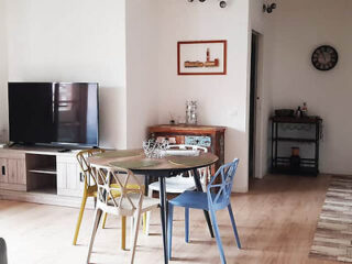A simple yet stylish dining area with a wooden table, colorful chairs, and a rustic sideboard, complete with a flat-screen TV and decorative elements
