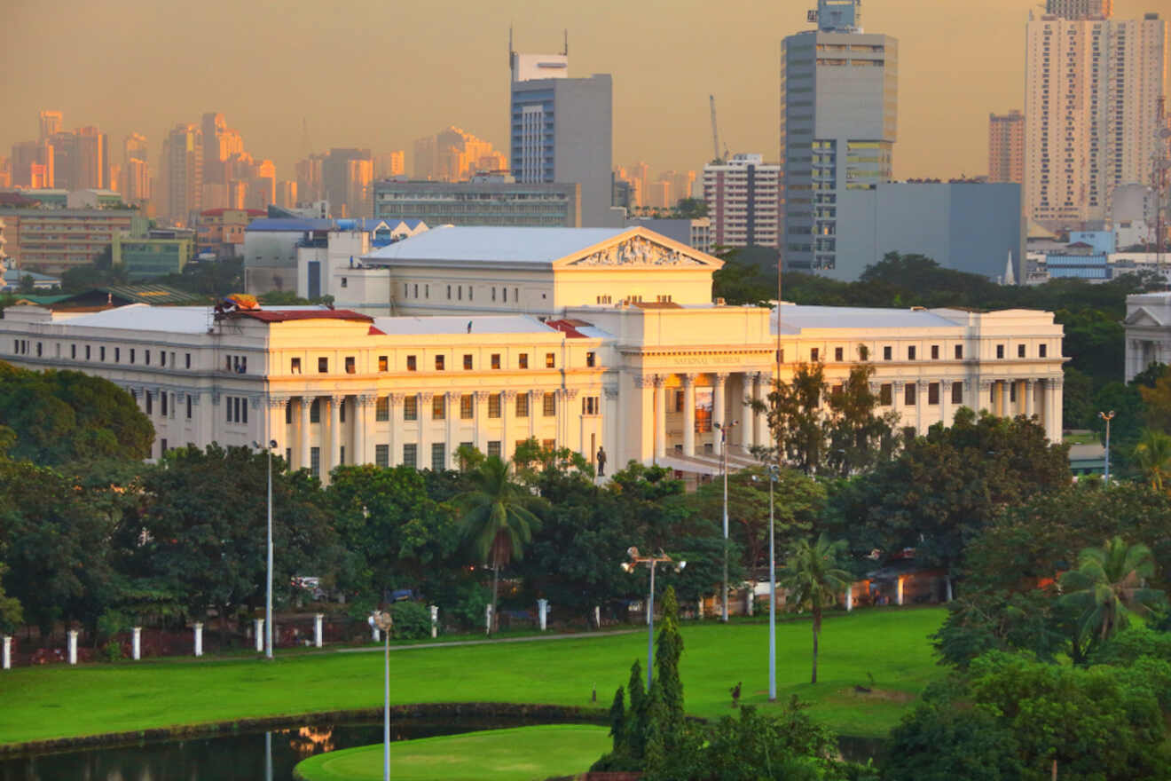 Sunset view of the National Museum of the Philippines with a lush green lawn in the foreground and a hazy city skyline in the background