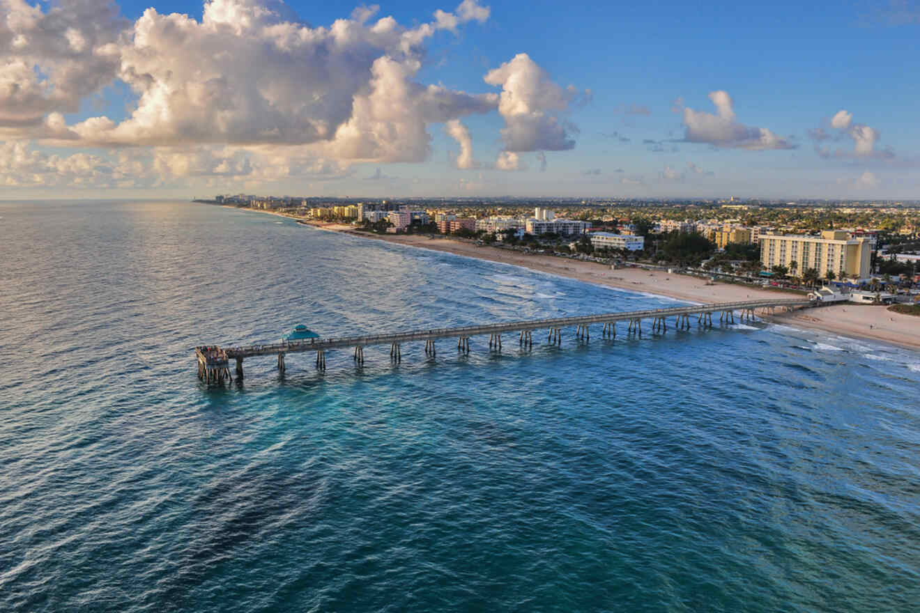 Morning light bathes a wooden pier extending into the ocean, with the beach and coastal buildings in the background