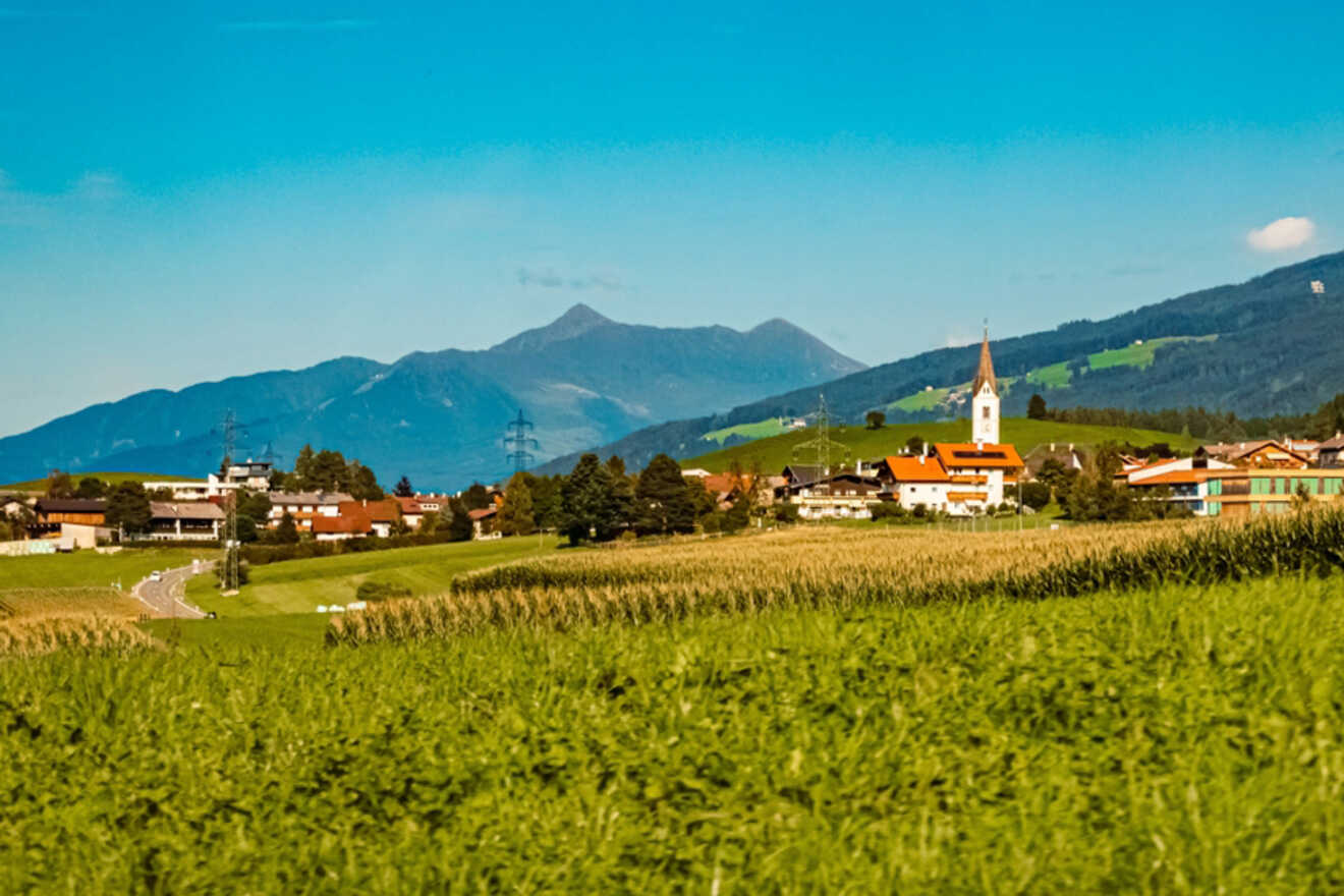 A scenic view of the rural village of Lans with a prominent church spire, set against a backdrop of rolling hills and clear blue skies