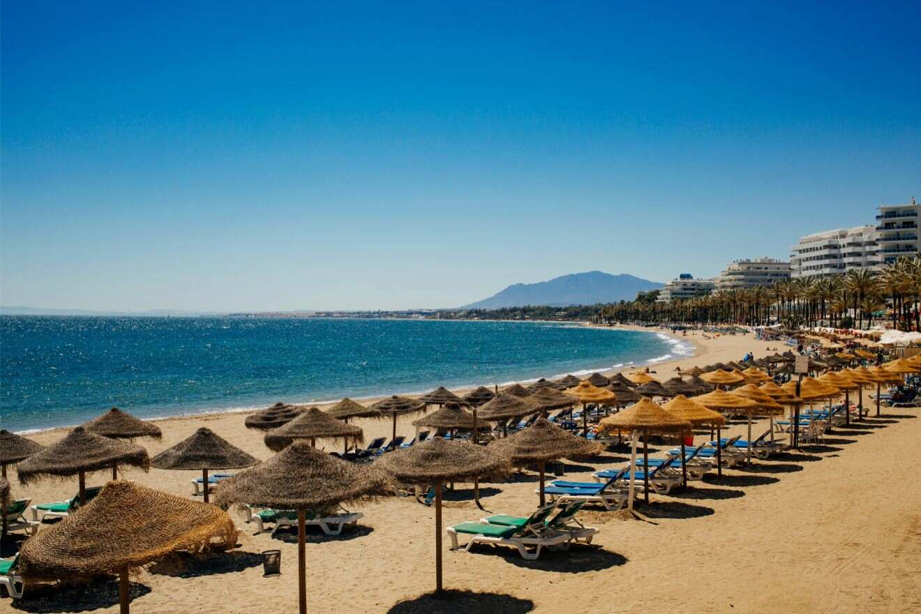 Sandy beach in Marbella, Cartagena with rows of straw umbrellas and sun loungers facing the blue waters, under a clear sky