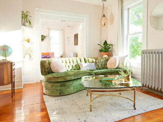 Bright living room with a plush green velvet sofa, large windows, and a vintage glass-top coffee table