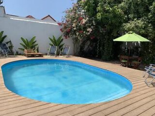 Secluded outdoor pool with wooden decking and a green patio umbrella, nestled within a private garden