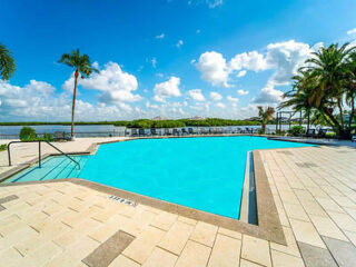 Resort-style pool on the waterfront with ample sun loungers, palm trees, and a view of the bay