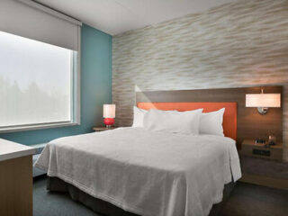Modern hotel room with a white bed, wood-paneled headboard, textured wall, and a warm-toned bedside lamp