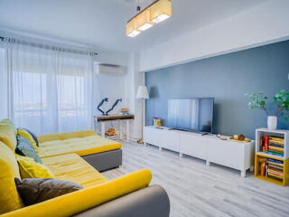A bright and airy living room with a large yellow sectional sofa, modern decor, and a sleek flat-screen TV