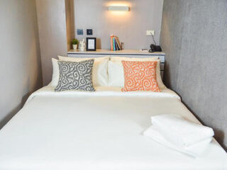 Minimalistic hotel room with a large double bed adorned with two decorative pillows against a textured gray wall
