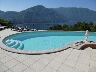 Curved infinity pool overlooking Lake Como with mountains in the distance, sun loungers on the side, and a statue as a focal point