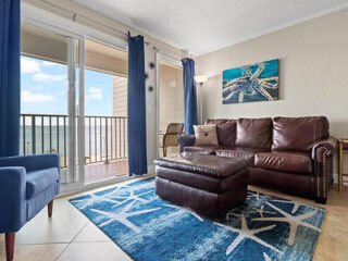 Seaside living room with balcony access, a brown leather couch, and a vibrant blue sea-themed rug
