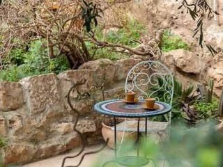 Quaint garden seating area with a wrought iron table and chairs set on a rustic stone patio surrounded by greenery.