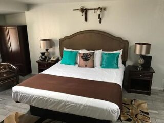 A sophisticated bedroom with a large bed adorned with a chocolate brown runner, teal accent pillows, and elegant bedside lamps