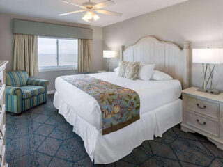 Coastal-inspired hotel room with a king-sized bed, striped armchair, and oceanfront view through large windows