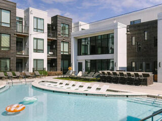Contemporary outdoor pool area with sun loungers and a semi-circular pool bench, flanked by modern apartment buildings