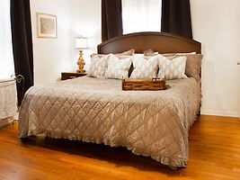 Classic bedroom with a large, dark wood bed frame and beige quilted bedding, complete with multiple pillows and hardwood flooring
