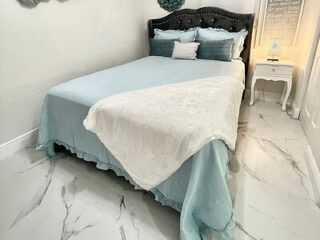 Chic bedroom with a light blue bedspread, white fur throw, and elegant gray tufted headboard