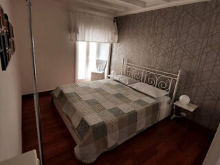 Simple bedroom with a metal frame bed, quilt cover, patterned wallpaper, and natural light streaming in from a window