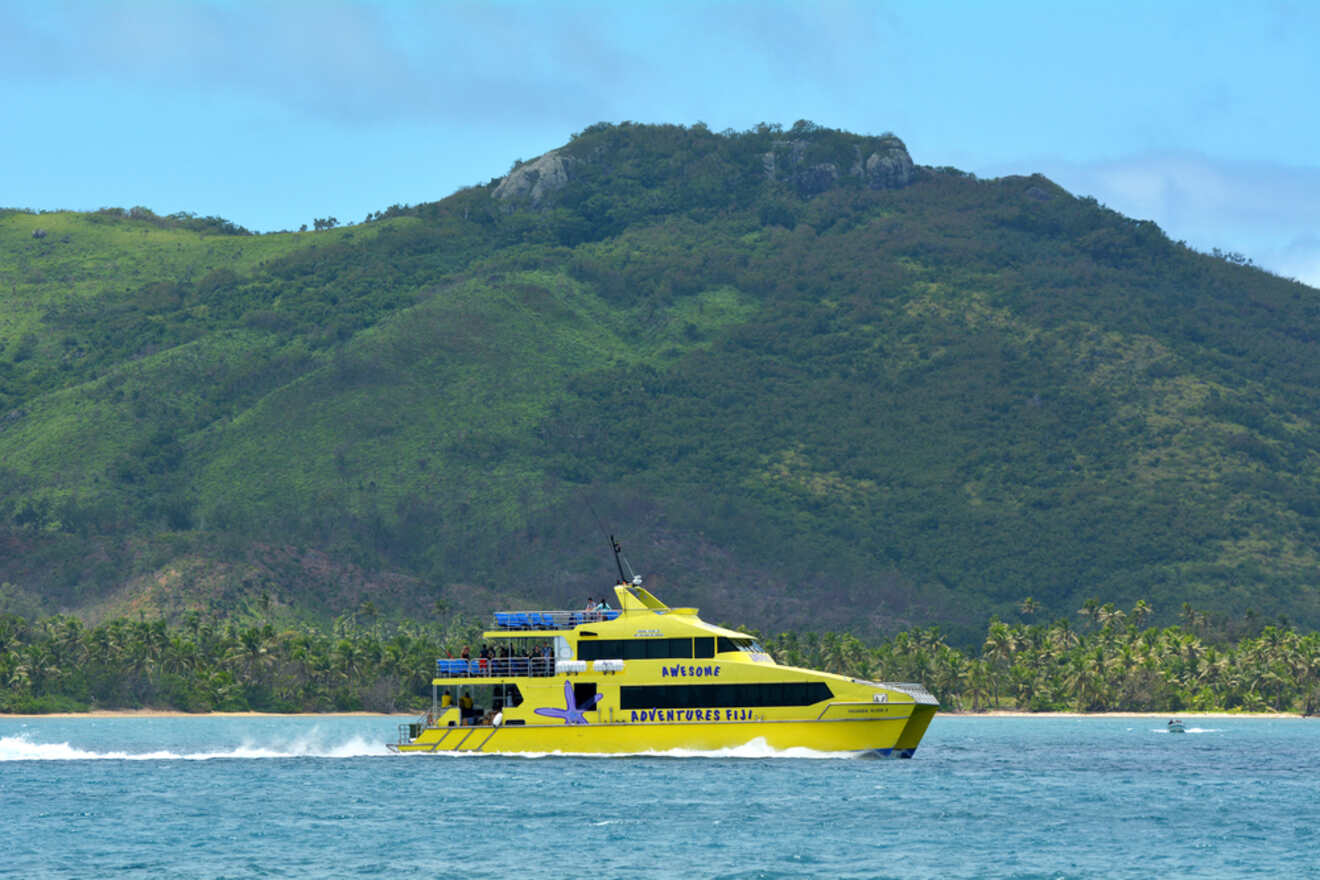 A bright yellow high-speed ferry marked "Awesome Adventures Fiji" cruising near a tropical island with lush greenery and palm trees