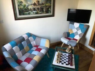 A bright living space with eclectic patchwork armchairs, a chess set on a coffee table, and a scenic painting on the wall